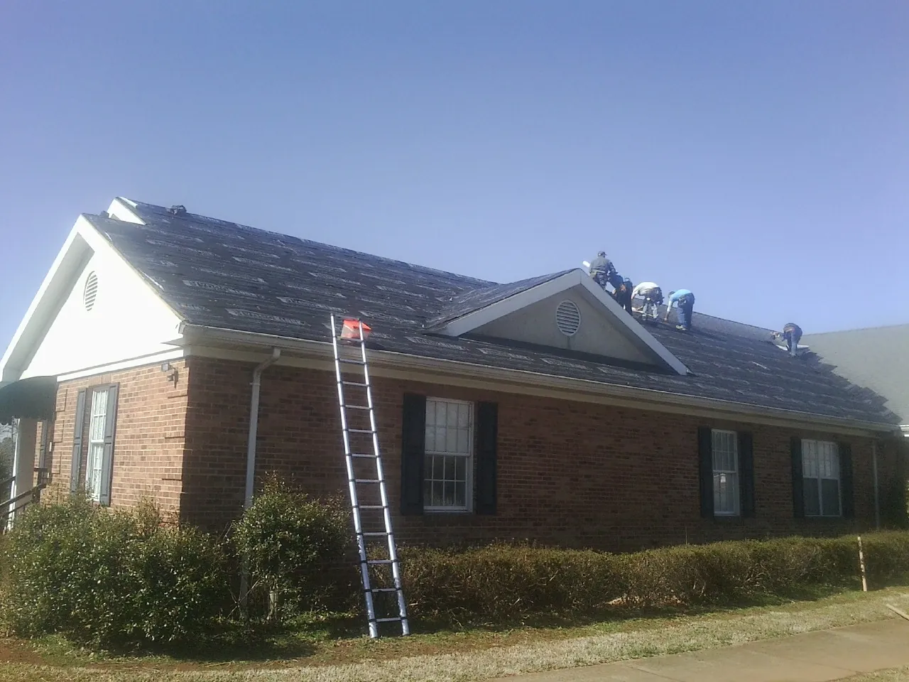 Crew tearing shingles off a brick ranch roof with a ladder set — Metal Roof Repair work by our crew in Laporte