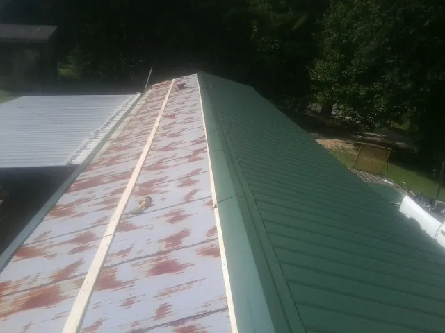 Old rusted panels beside newly installed green metal roofing — Wind Damage Roof Repair by Roofing Brothers in Laporte