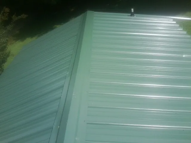 New green metal panels meeting at the ridge of a roof — Flat Roof Repair work by our crew in Laporte