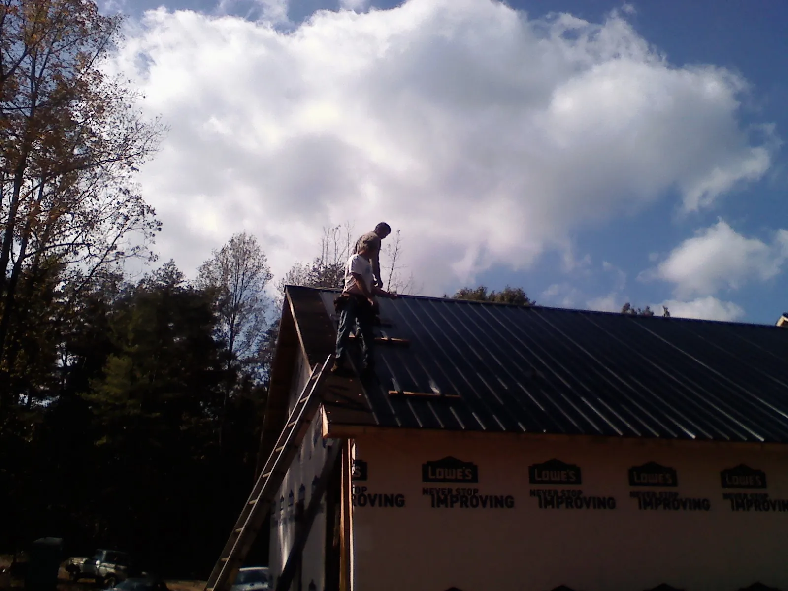 Roofer fastening dark metal panels high against a cloudy sky, from a Roof Inspection job in Laporte